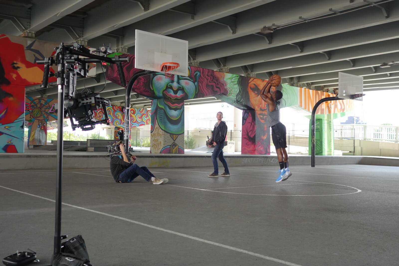 A camera rig set up at a covered outdoor basketball court beneath a graffitied overpass