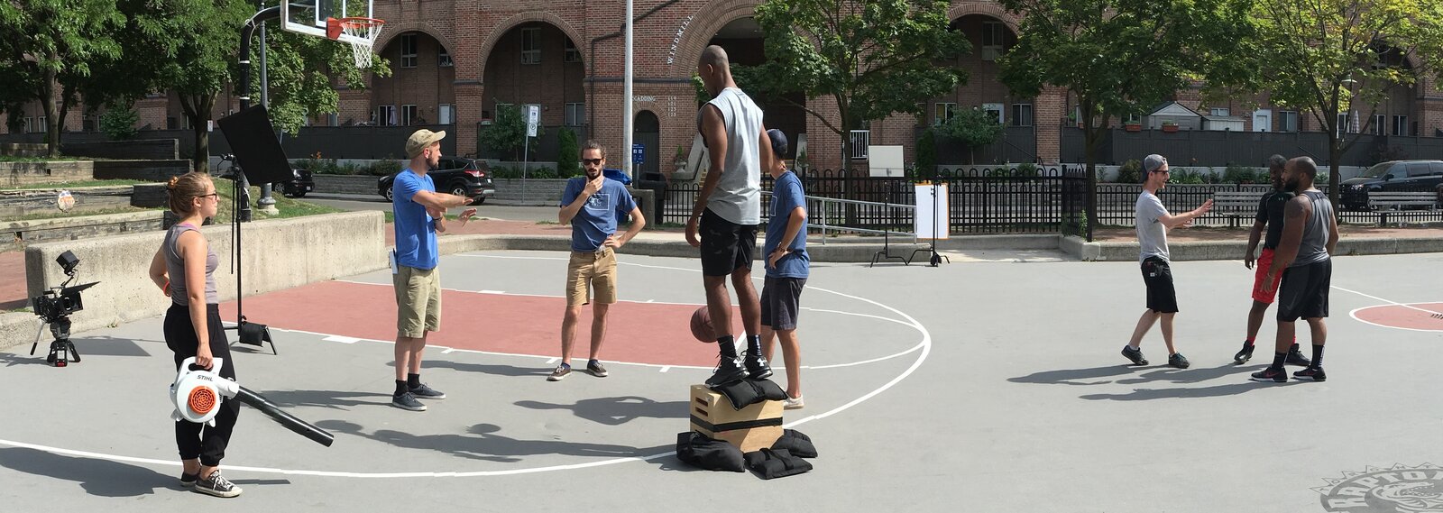 An ultra-wide frame of the outdoor court, crew and players in shot